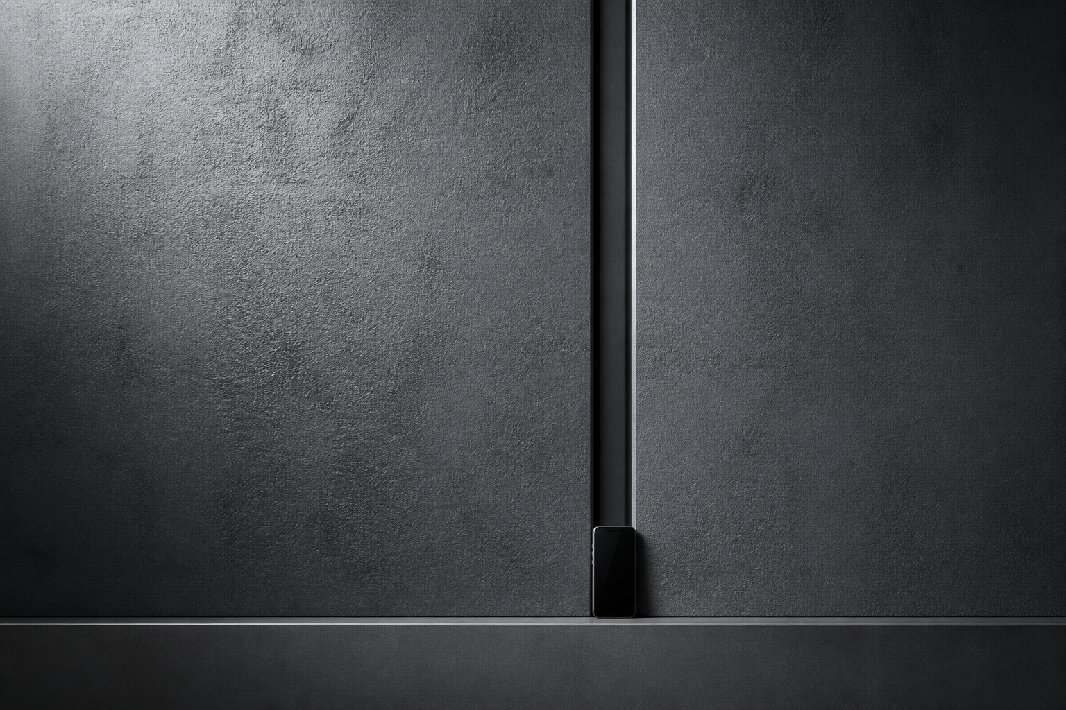 A dark machined graphite wall with a narrow central datum and a small device seated at its base.